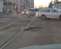 На фото видно яму и углубление ливневки, что затрудняет движение автотранспорта, также на это участке дороги по трамвайным путям около рельс большие выбоины.